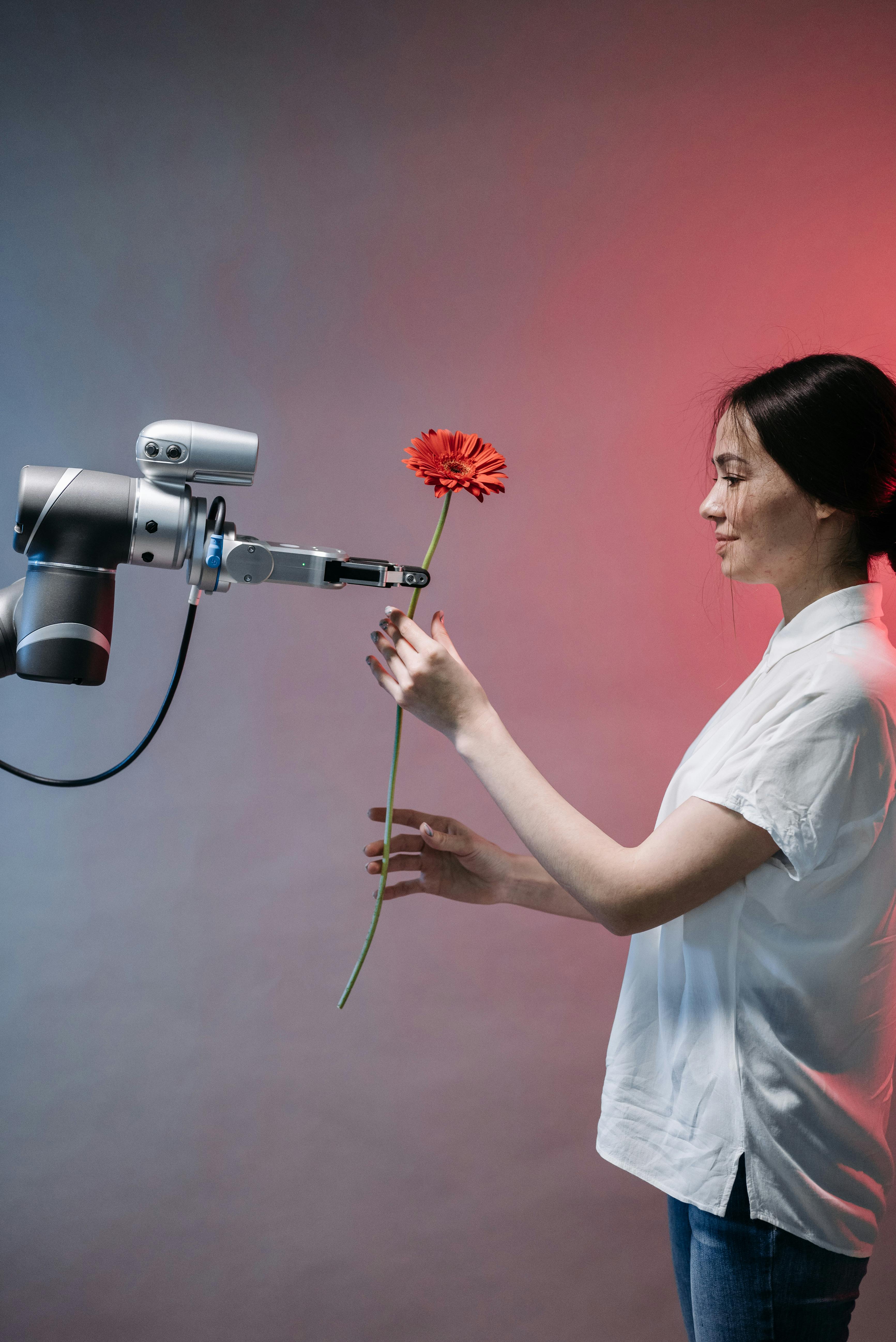 pexels-photo-8438979-8438979 A woman interacts with a robotic arm holding a flower, symbolizing human-technology harmony.